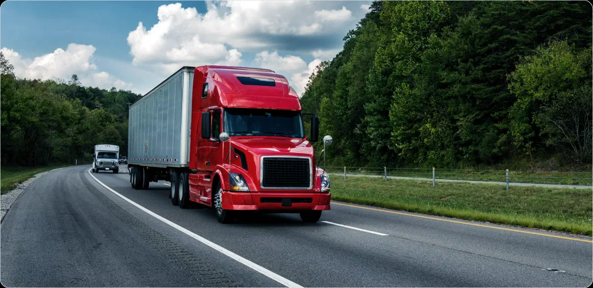 A red semi truck hauling a trailer on a tree-lined interstate